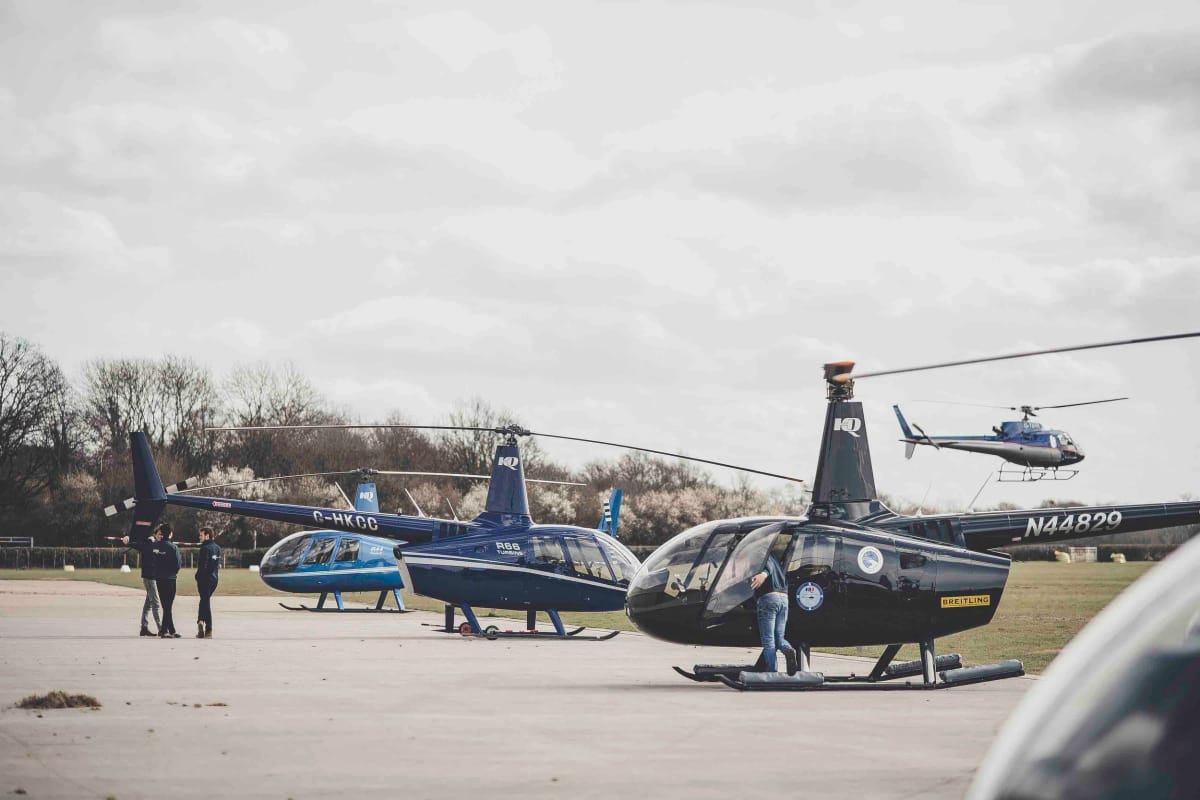HQ Aviation crew on the apron at Denham with three Robinson helicopters and one lifting off behind them