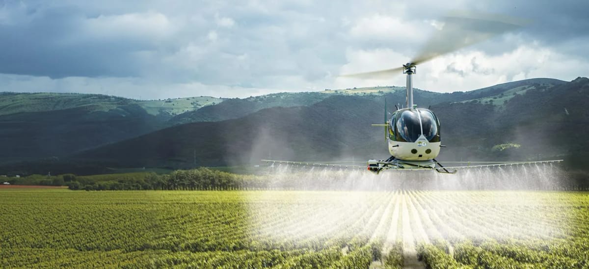 Robinson R44 Sprayhawk unmanned helicopter spraying a crop field